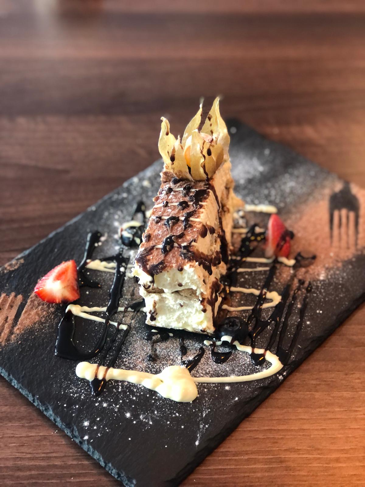Tiramisù dessert dusted with cocoa and drizzled with chocolate, plated on slate